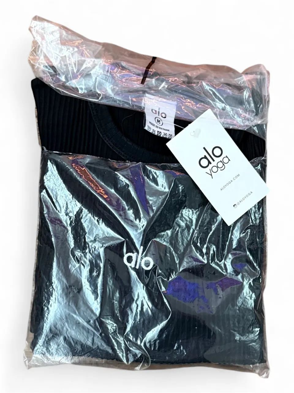 vestido corto manga larga de mujer, de la marca Alo Yoga, de color negro, con cuello redondo y detalle del logo de la marca en el frente. Ideal para actividades deportivas o uso casual.