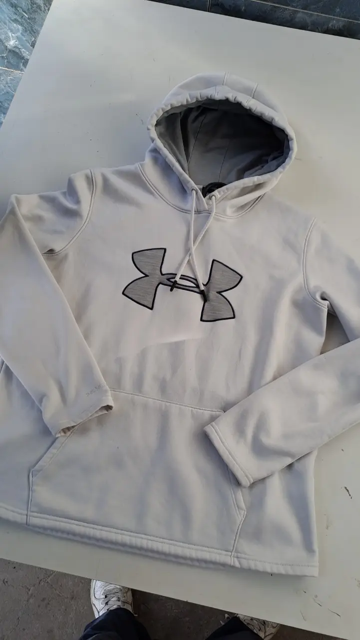 Buzo canguro Under Armour blanco con logo gris. Interior de polar, ideal para el invierno. Perfecto para un look casual y abrigado.
