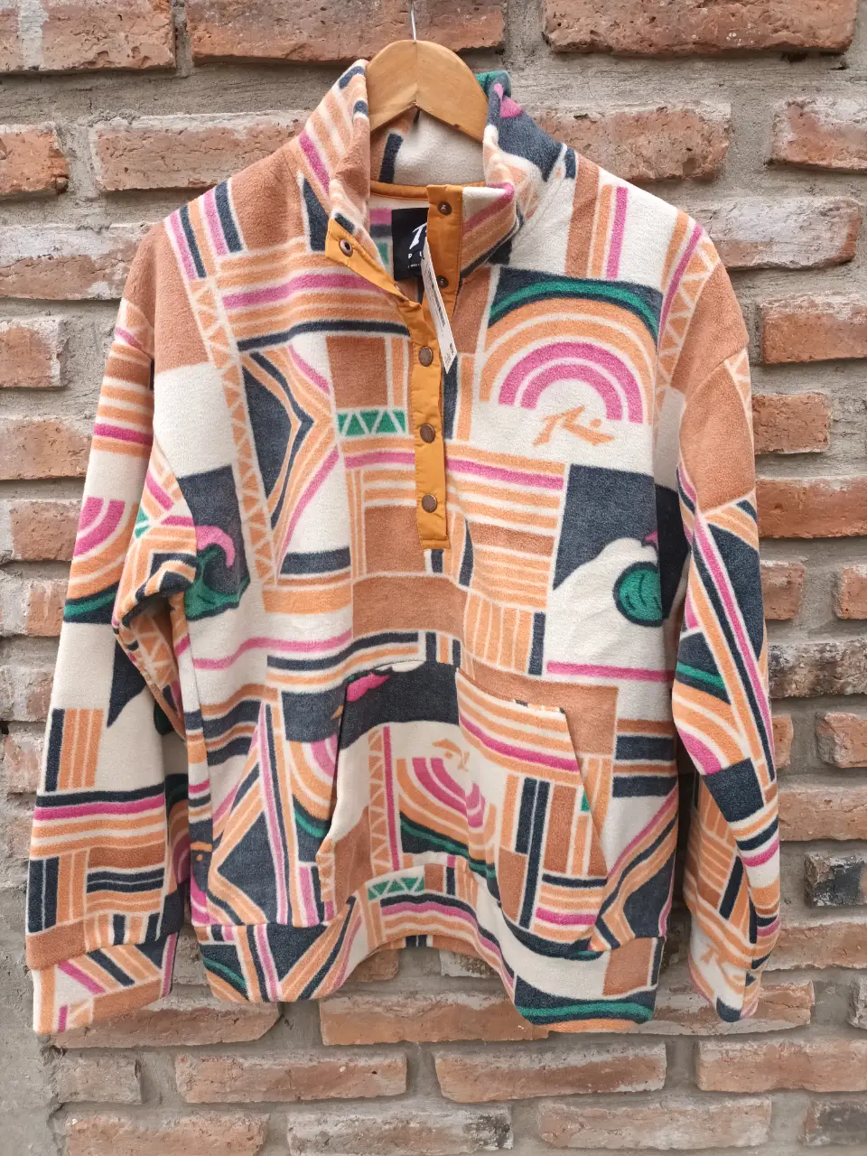 Buzo polar con cuello alto y botones, estampado geométrico en tonos tierra, naranja, rosa y verde. Ideal para un look casual y abrigado.