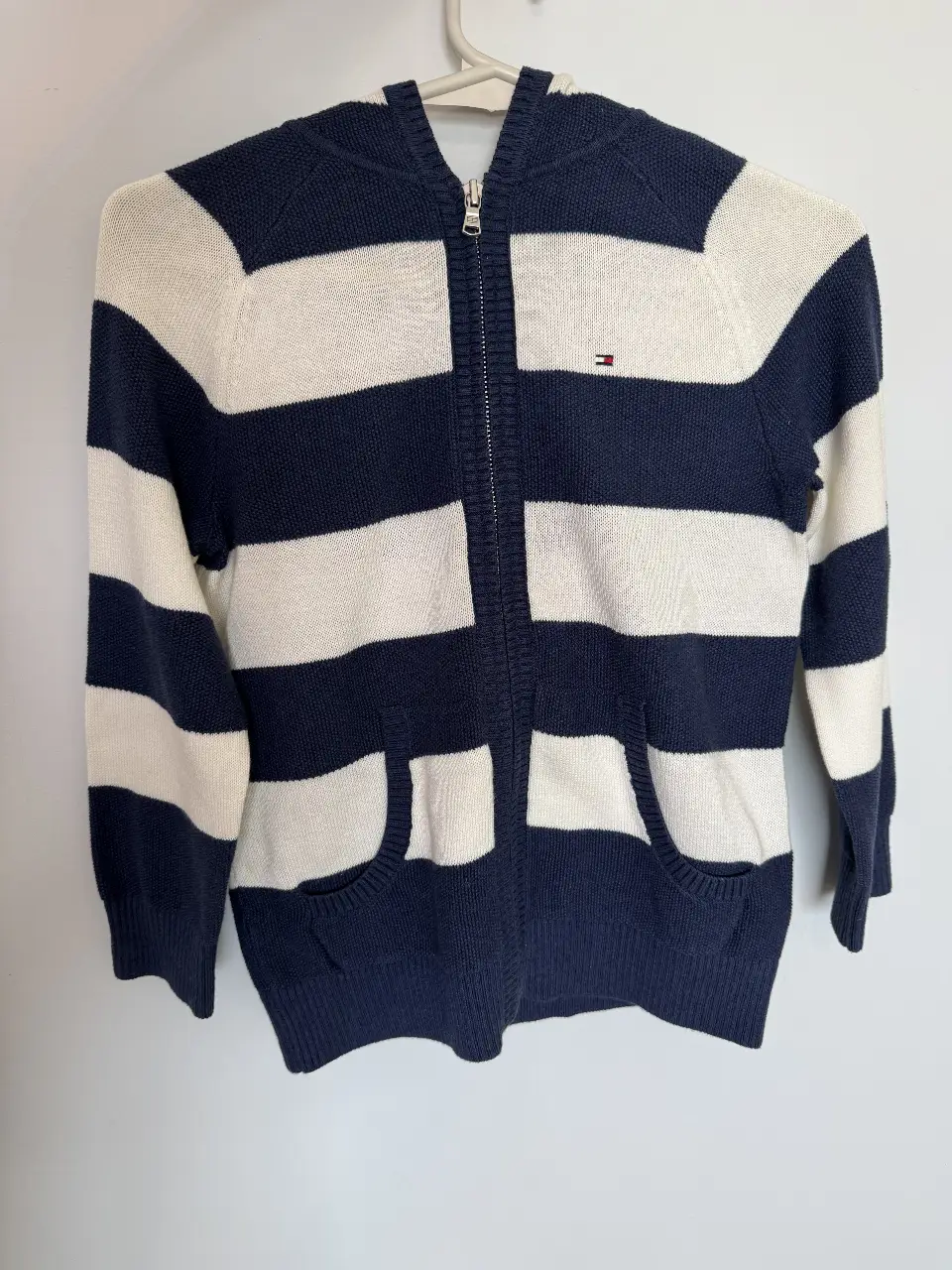 Buzo con cierre para niño, a rayas horizontales en azul y blanco, con capucha y bolsillos delanteros. Logo de Tommy Hilfiger en el pecho.