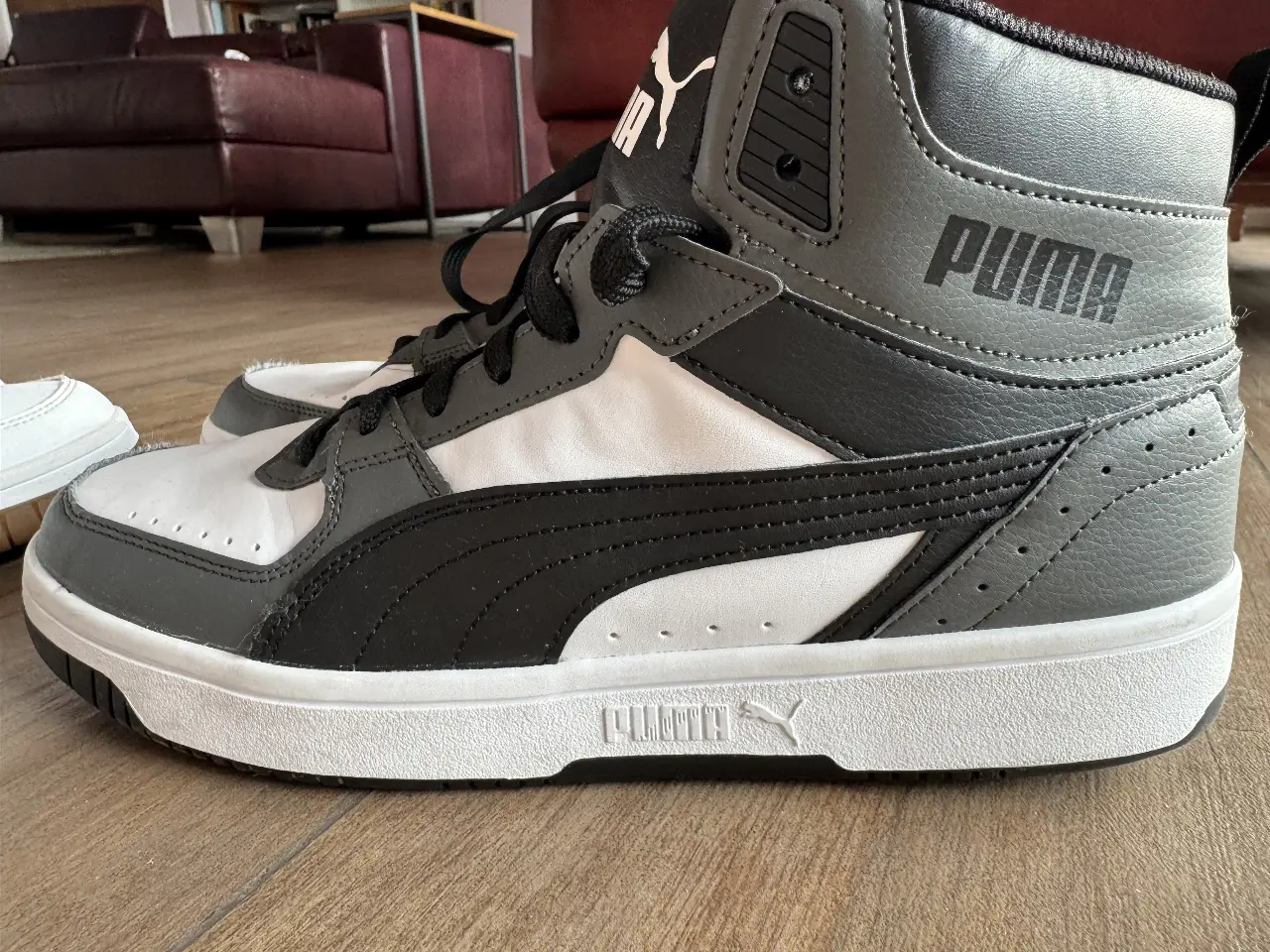 Zapatillas Puma Rebound JOY unisex, alta moda retro, en color blanco, gris y negro. Ideales para un look urbano y deportivo.