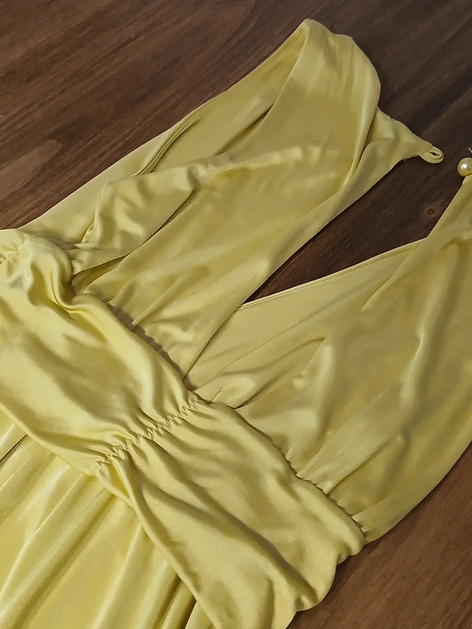 Vestido largo amarillo con escote en V profundo y detalle de lazo en la cintura. Posee tiras finas en la espalda que se unen con un detalle de perla.