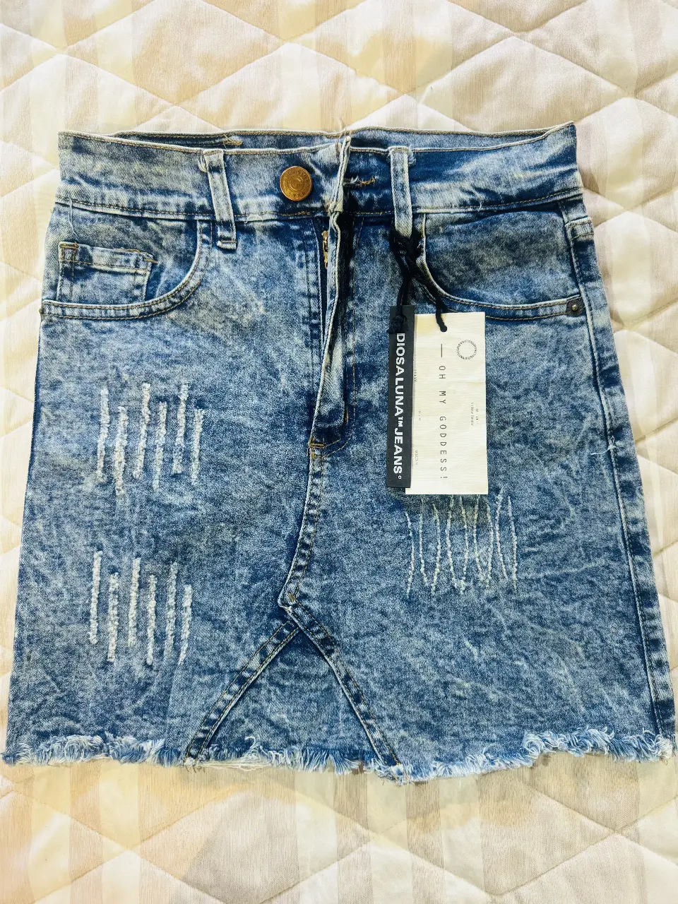 Minifalda de jean azul con detalles desgastados y roturas. Ideal para un look casual y moderno. Marca Diosa Luna Jeans. 38cm de largo y 31cm de cintura. Elastizada.
