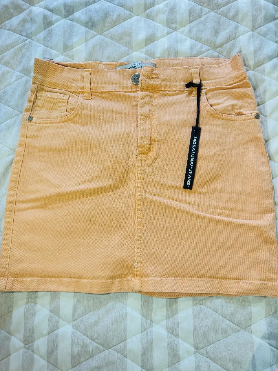 Pollera de jean color durazno, tiro medio, con bolsillos delanteros y traseros. Ideal para un look casual y fresco. 39cm de largo y 36cm de cintura.