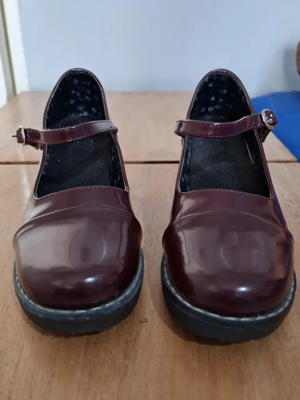 Zapatos tipo Mary Jane de charol color borgoña, con hebilla en el tobillo y suela negra.