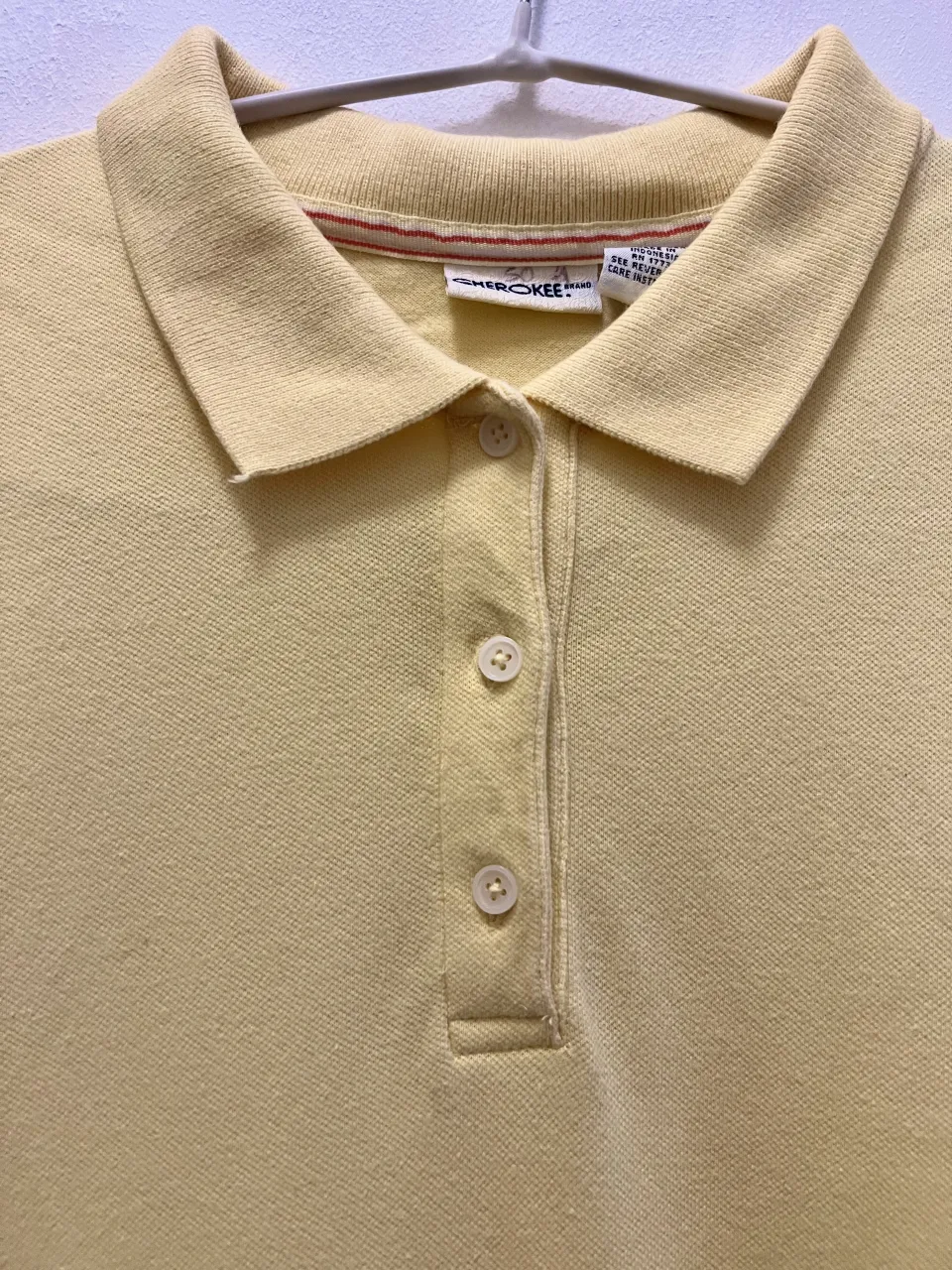 Remera polo amarilla de manga corta con cuello y tres botones en la parte superior. La marca 'Cherokee' es visible en la etiqueta.