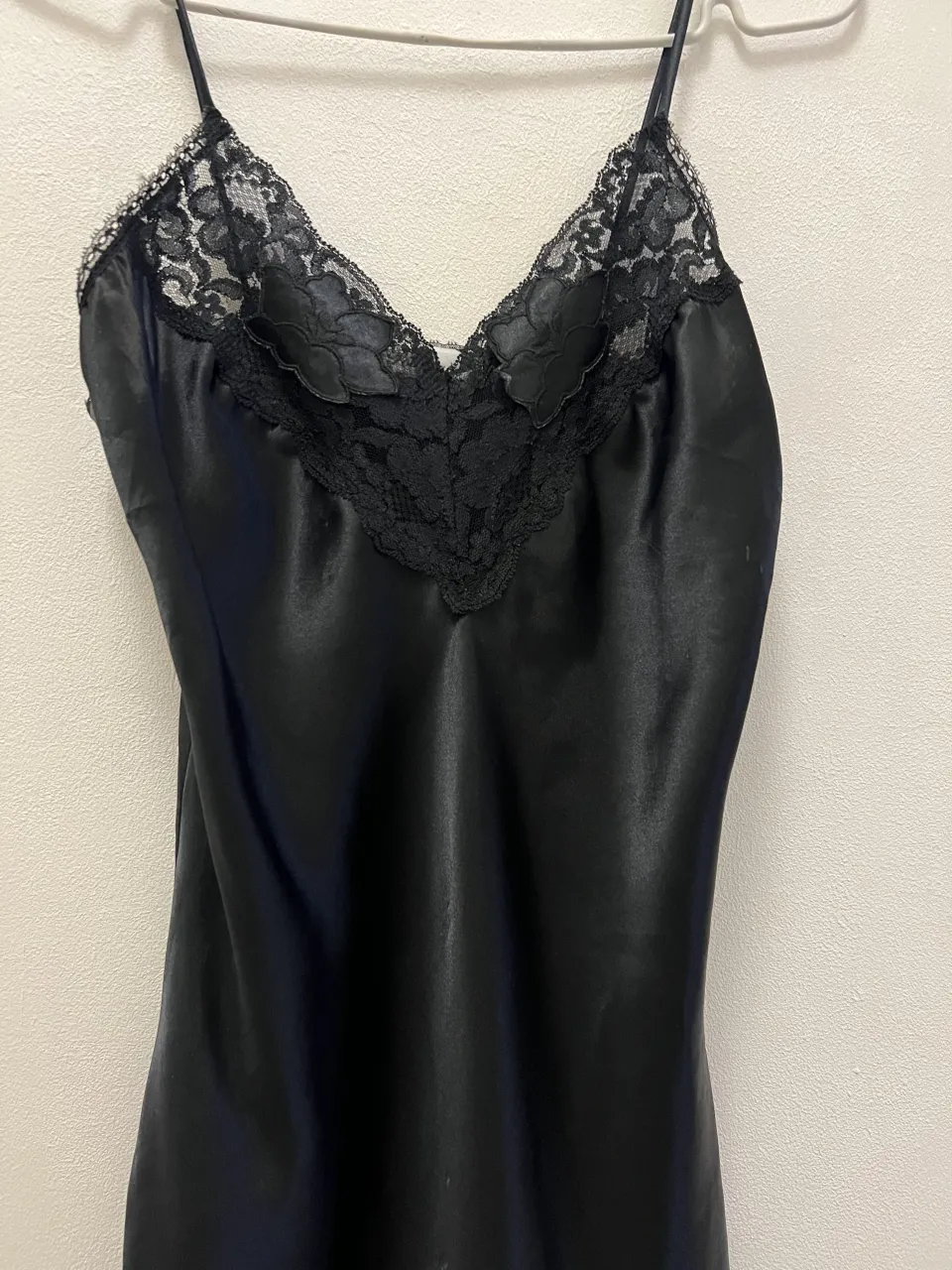 Vestido negro de satén con detalles de encaje en el escote y breteles finos.