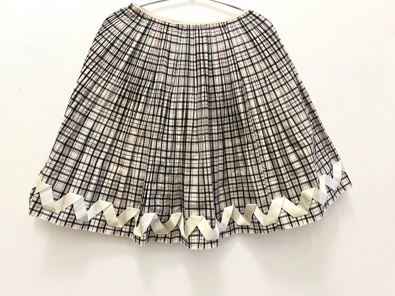 Pollera a cuadros escoceses con detalle de cintas blancas en el ruedo. Cierre en la espalda.