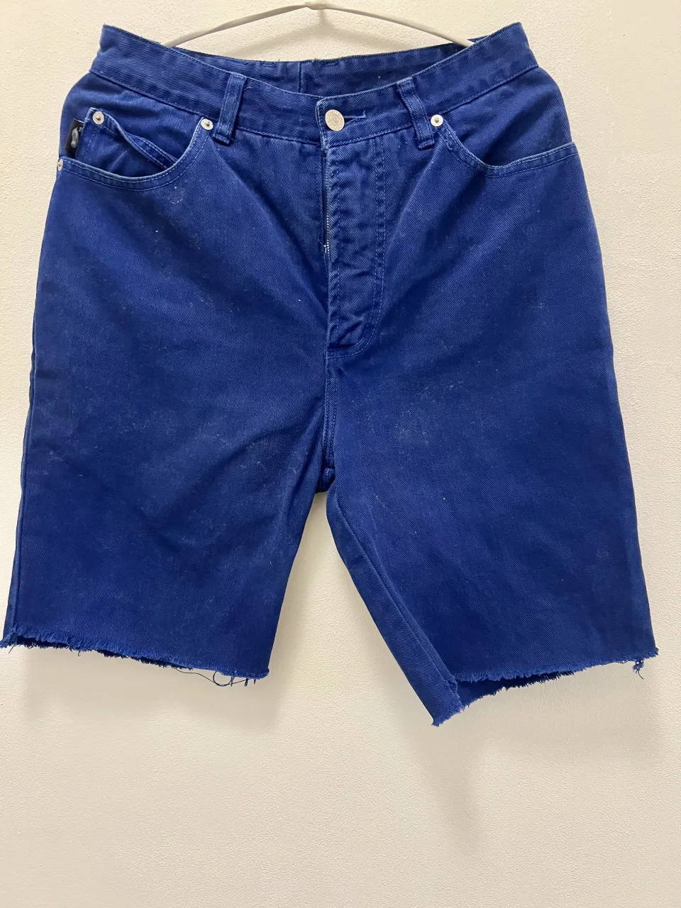 Shorts de jean azul con borde deshilachado. Tienen bolsillos delanteros y traseros.