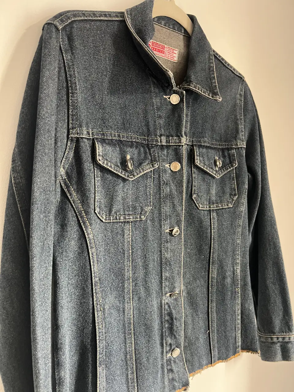 Campera de jean azul oscuro, con detalles de costura en contraste y botones plateados. Corte clásico con bolsillos delanteros y un estilo vintage.