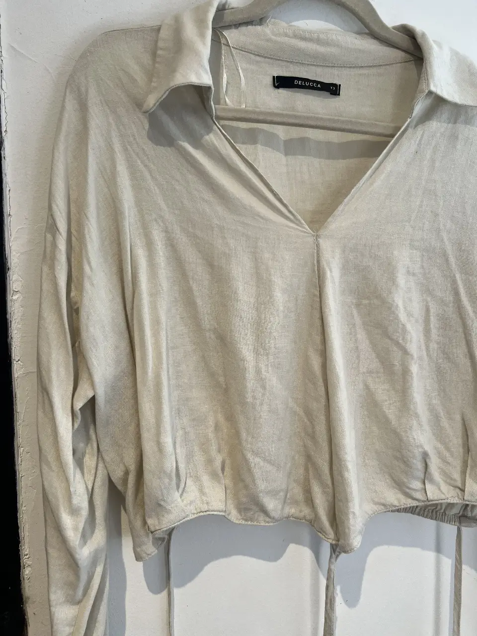 Blusa de mujer color crudo, con cuello camisero y escote en V. Manga larga y detalle fruncido en la cintura. Ideal para un look casual y elegante.