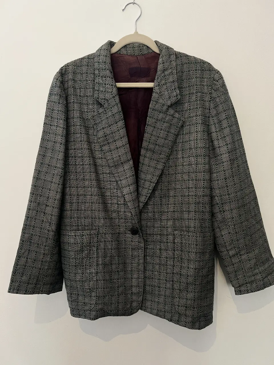 Blazer de hombre vintage, gris con diseño a cuadros. Corte clásico, con dos bolsillos frontales y un botón para cerrar. Ideal para un look elegante y atemporal.