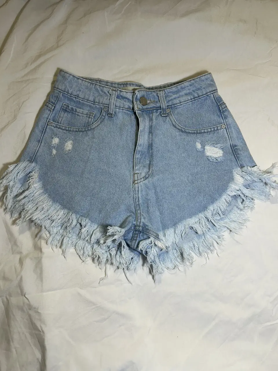 Short de jean de mujer, tiro medio, con detalles de roturas y flecos en el borde inferior. Ideal para un look casual y moderno.