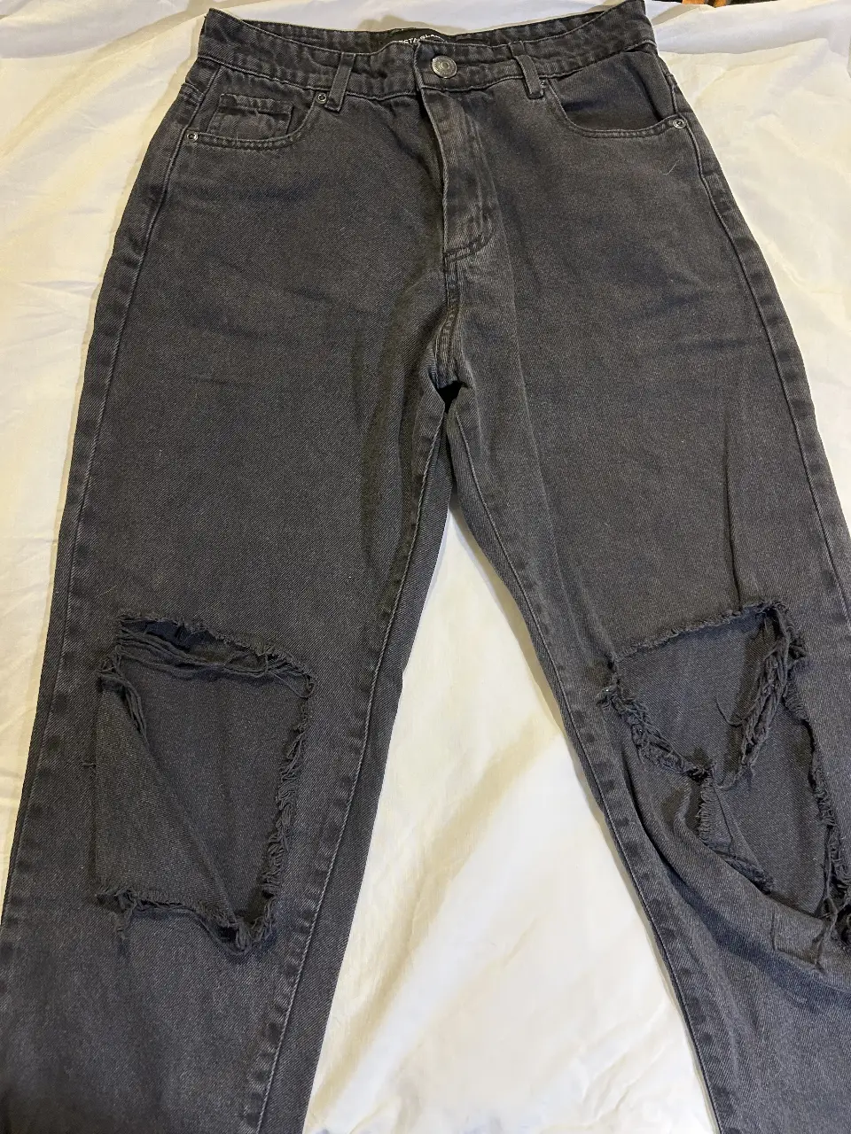 Jeans de mujer de color gris con roturas en las rodillas. Tiro alto, corte recto y con detalles de desgaste en los bordes. Ideal para un look casual y moderno.