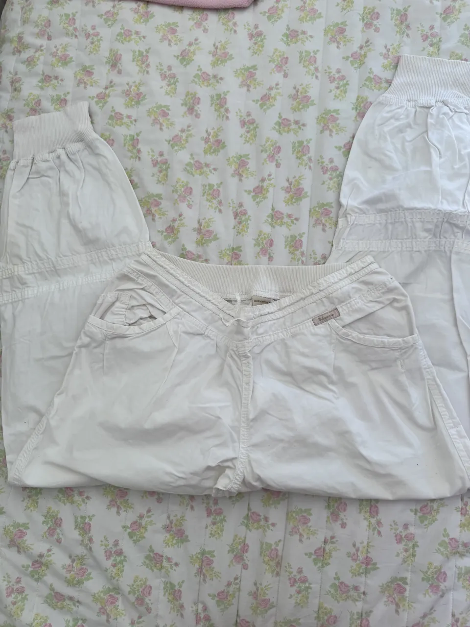 Pantalón blanco con cintura elastizada y cordón (tipo parachute) Posee bolsillos frontales y puños elastizados en los tobillos. Tiene una pequeña etiqueta de marca en el frente.