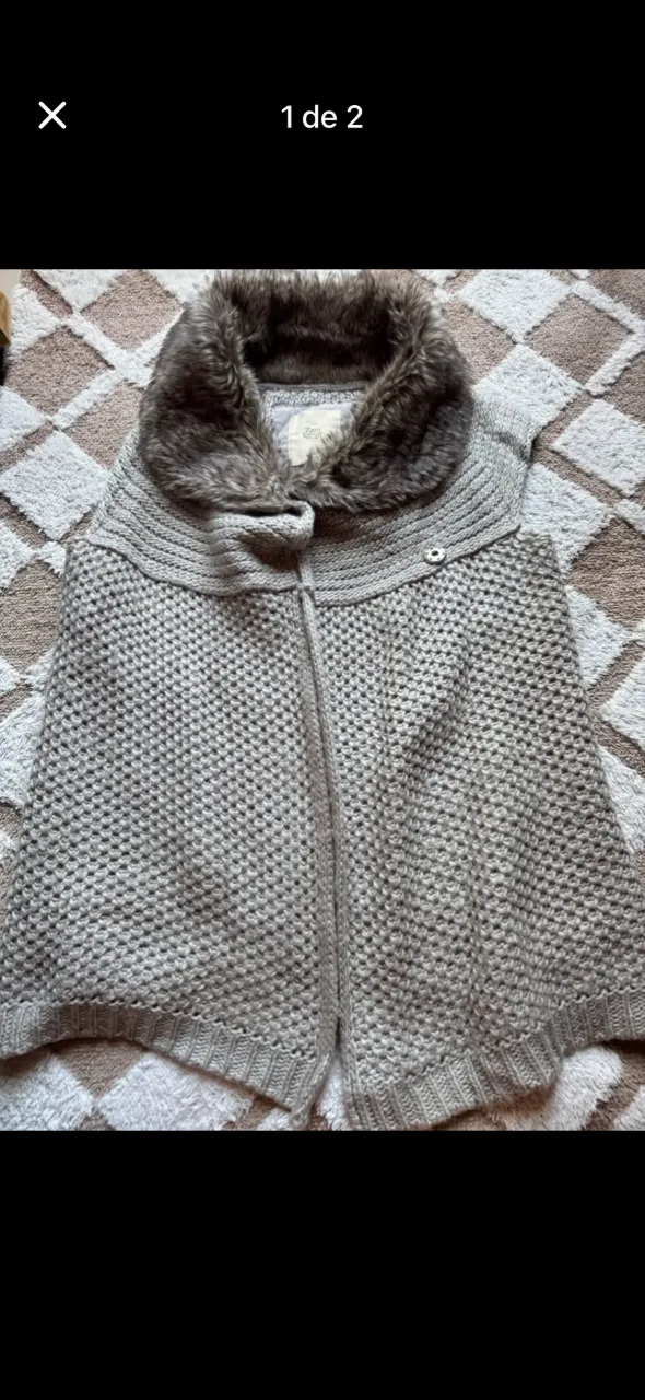 Chaleco tejido gris con cuello de piel sintética marrón. Cierre al frente con un botón.