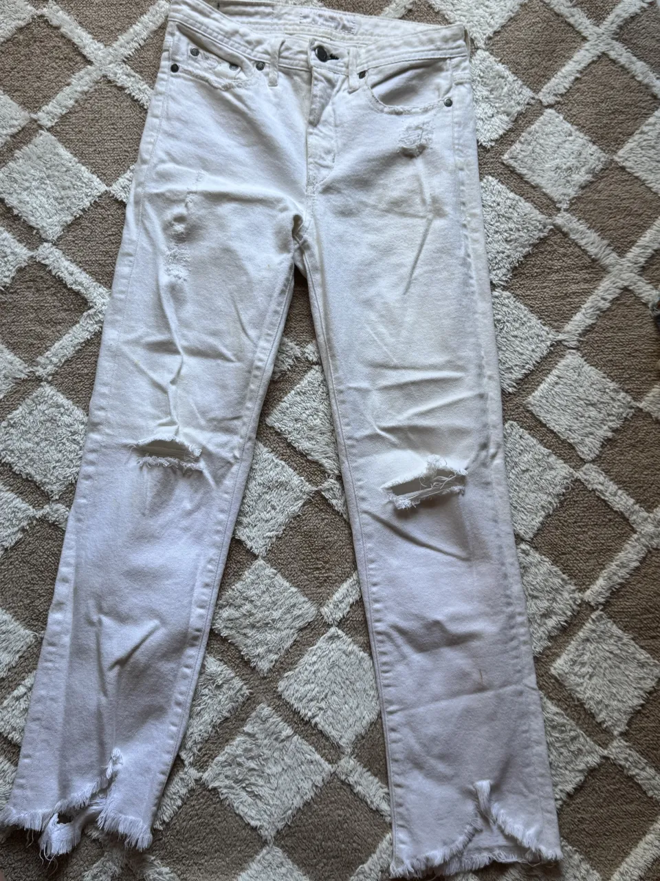 Jeans blancos con roturas y detalles deshilachados en los bajos.