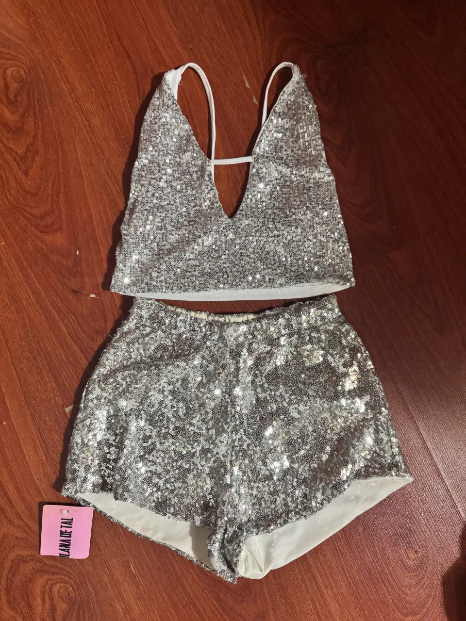 Conjunto de top y shorts plateados con lentejuelas. El top es corto, con escote en V y tiras finas. Los shorts son tiro alto y cortos.