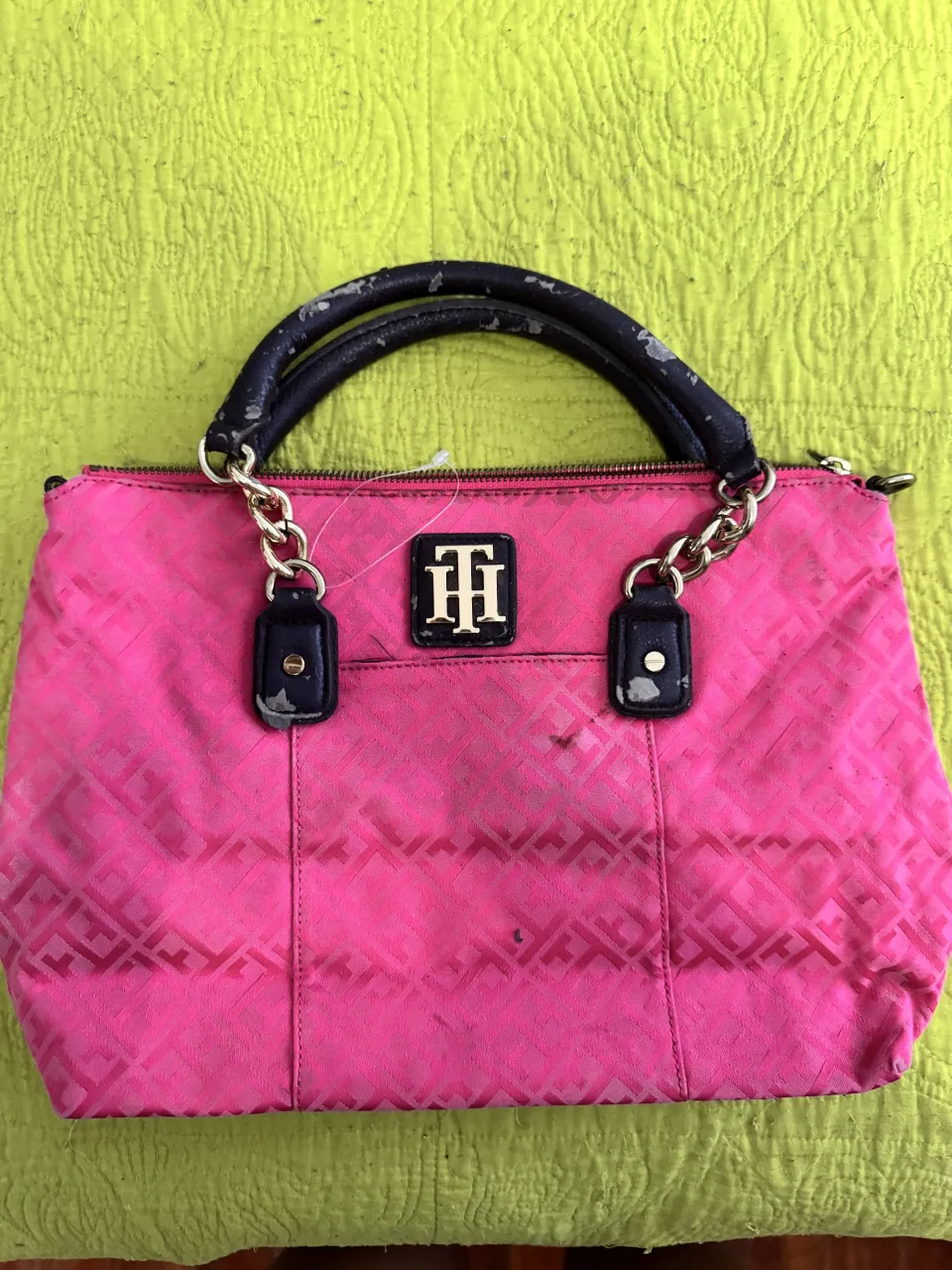 Cartera de color rosa con logo TH en dorado. Posee manijas negras y detalles en cadena dorada.