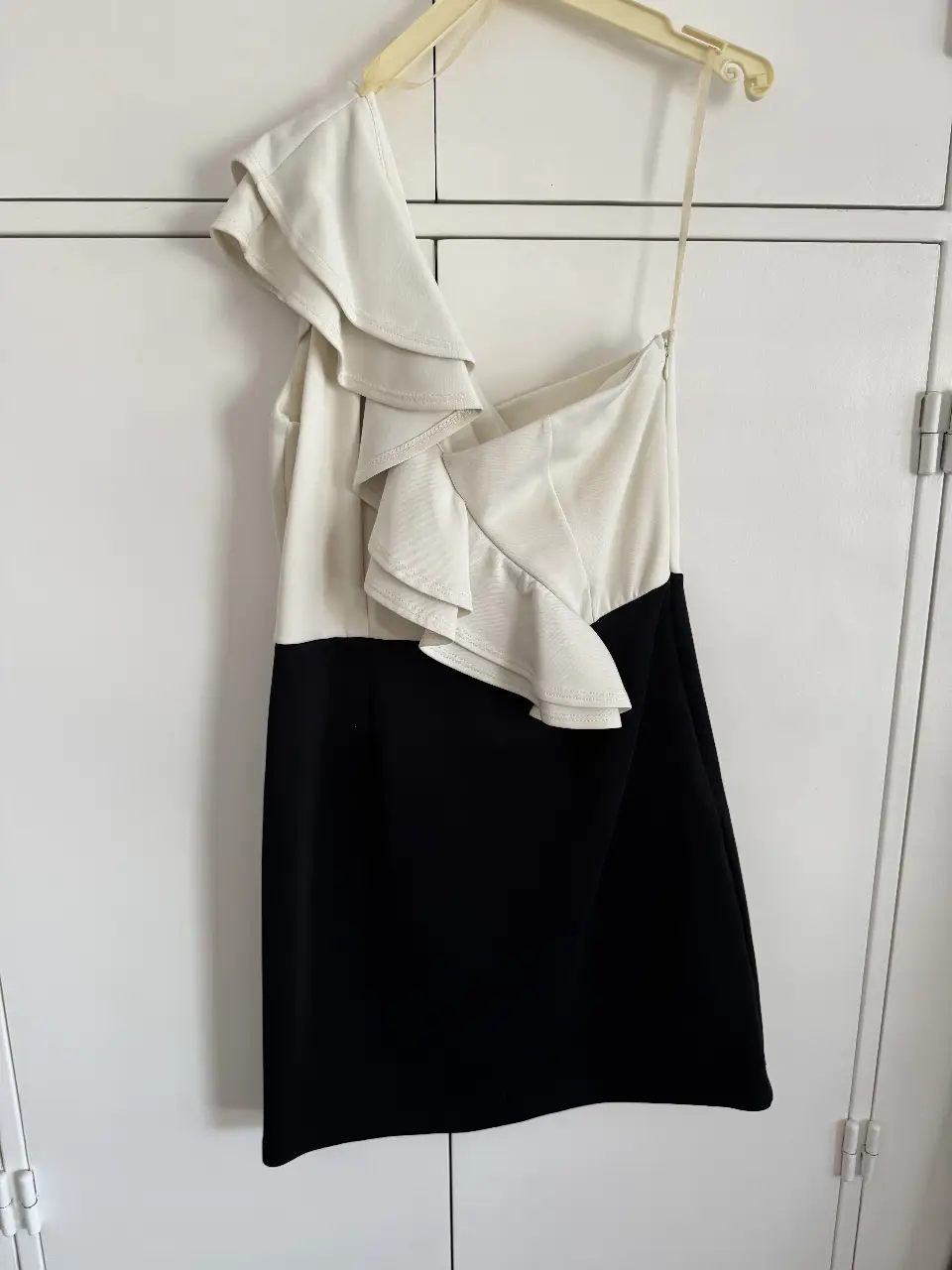 Vestido mini de fiesta, asimétrico, con un hombro descubierto y volados. La parte superior es blanca y la inferior negra. Ideal para eventos especiales.
