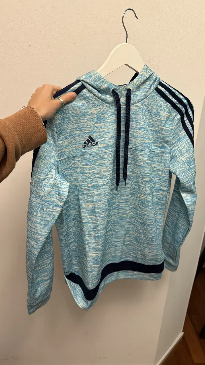 Buzo deportivo Adidas color celeste con detalles en azul marino. Con capucha y el logo de la marca en el pecho. Ideal para actividades deportivas o uso casual.
