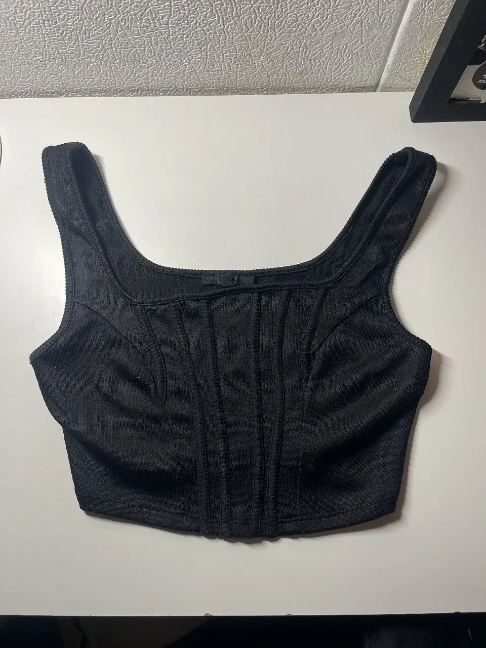 Top negro ajustado tipo corset de tela. Confeccionado con un tejido que se adapta al cuerpo, este top es perfecto para combinar con jeans, faldas o pantalones de vestir. Un básico imprescindible en tu guardarropa.