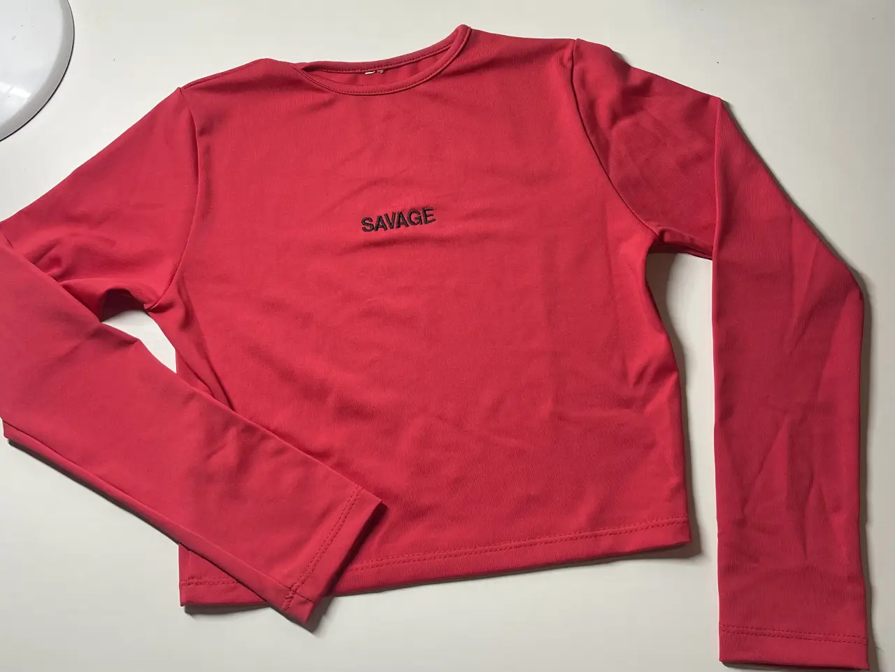 Remera manga larga roja con la palabra "SAVAGE" estampada en el frente. Ideal para un look casual y moderno.