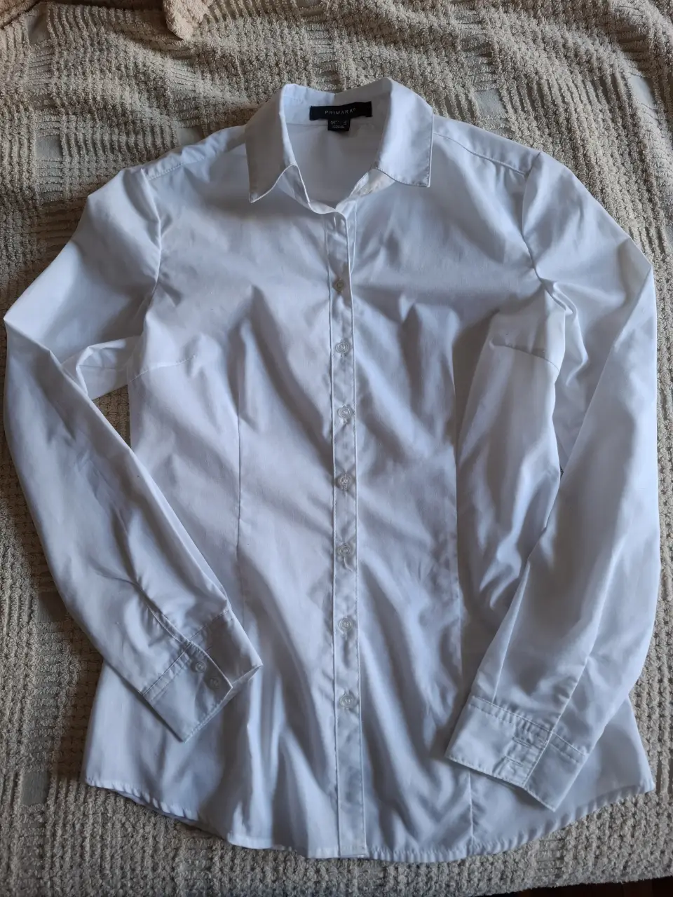 Camisa blanca de mujer, manga larga, con botones, cuello clásico y pinzas frontales que la hacen entallada. Ideal para un look formal o de trabajo.