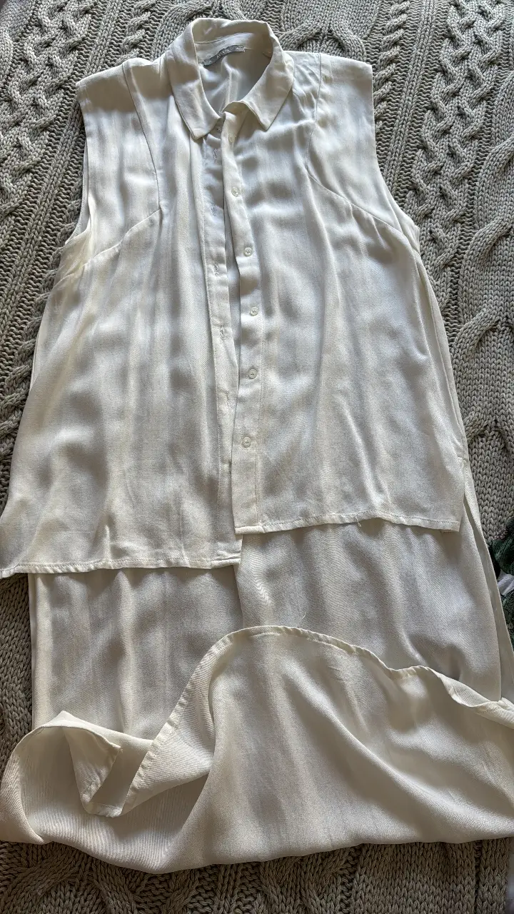 Blusa de mujer, color blanco, con cuello camisero y botones frontales. Diseño sin mangas y corte fluido, ideal para un look fresco y elegante.
