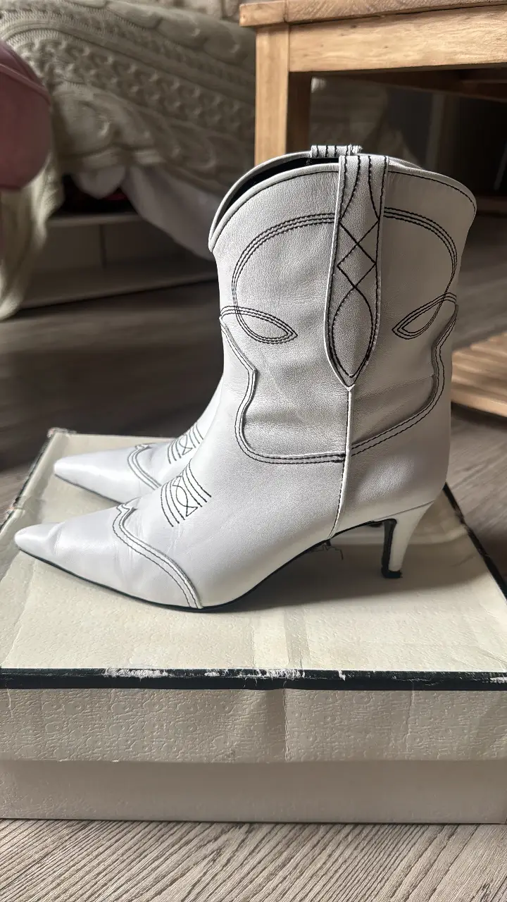 Botines blancos de cuero con detalles de costura negra. Diseño de punta fina y taco fino. Ideales para un look moderno y sofisticado.