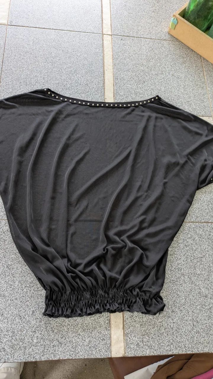 Remera negra con detalles de tachas plateadas en el cuello y puños. Posee fruncido elástico en la cintura.