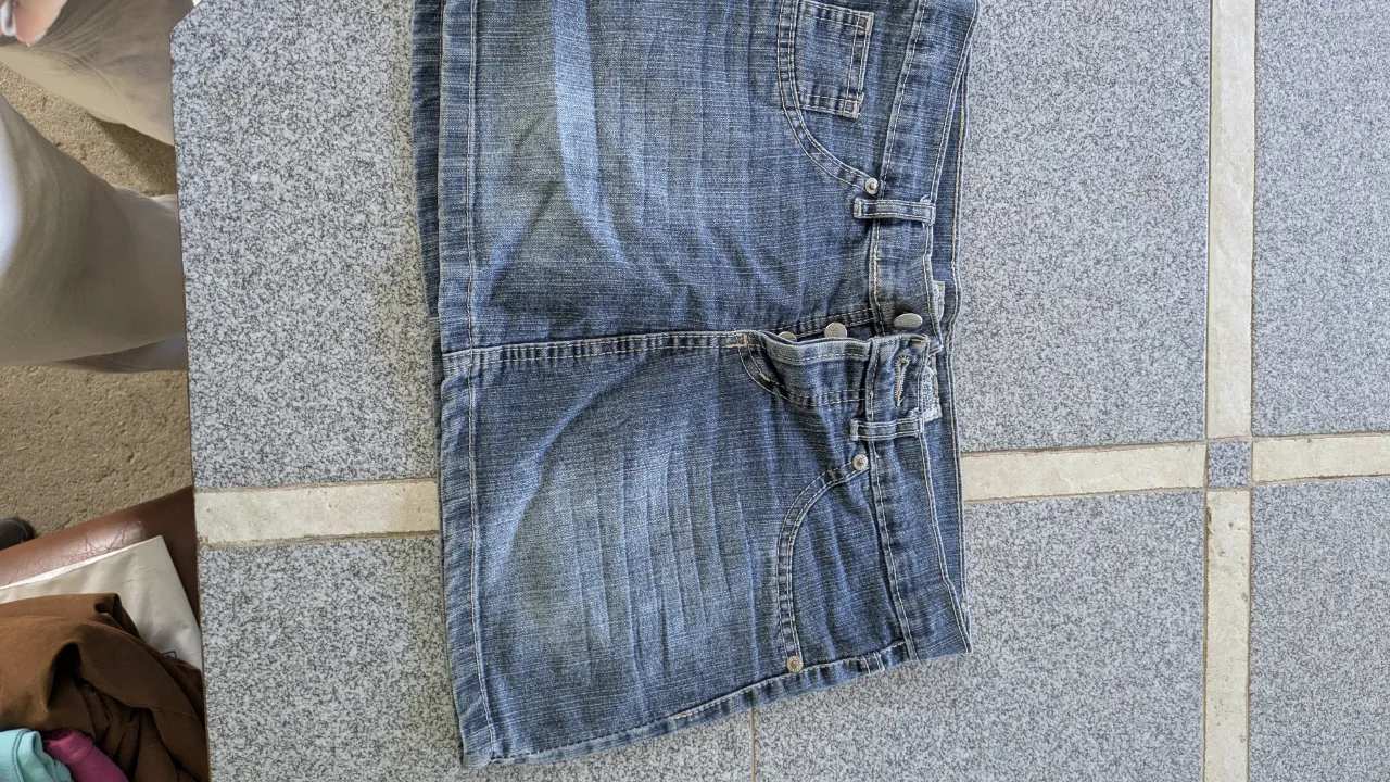 Jeans de denim azul con detalles de costura y un parche de cuero con el logo de la marca en la parte trasera. Presenta bolsillos delanteros y traseros, uno de ellos con un aplique de estrella metálica.