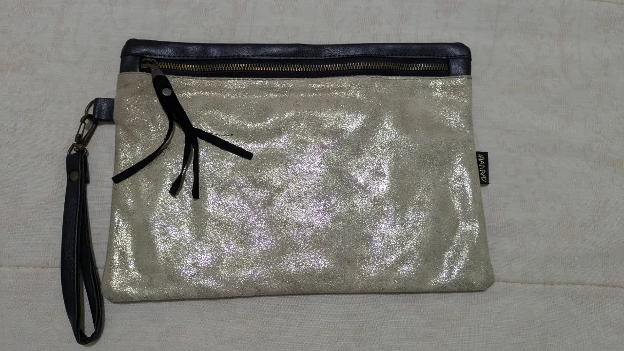 Clutch de mano para mujer, con exterior plateado brillante y detalles en negro. Posee cierre y correa para muñeca.