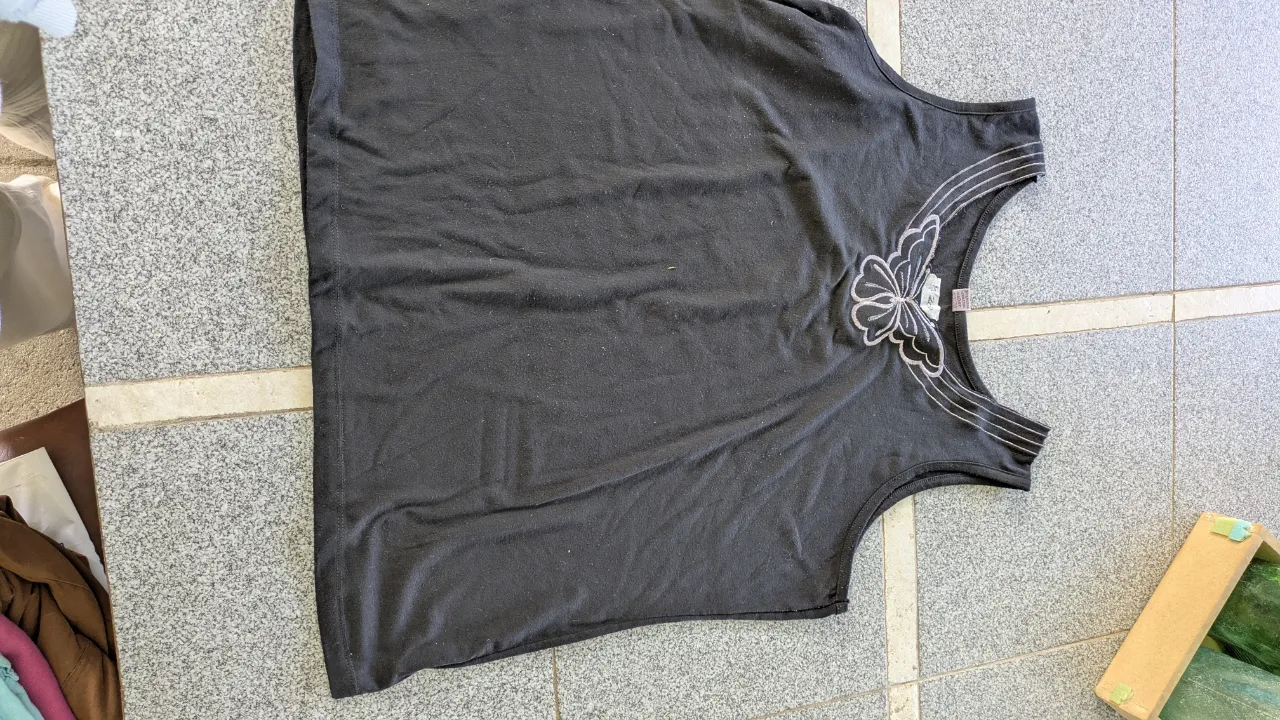 Musculosa negra con bordado de mariposa en la parte delantera. La mariposa está realizada en hilo plateado y blanco, con detalles brillantes.