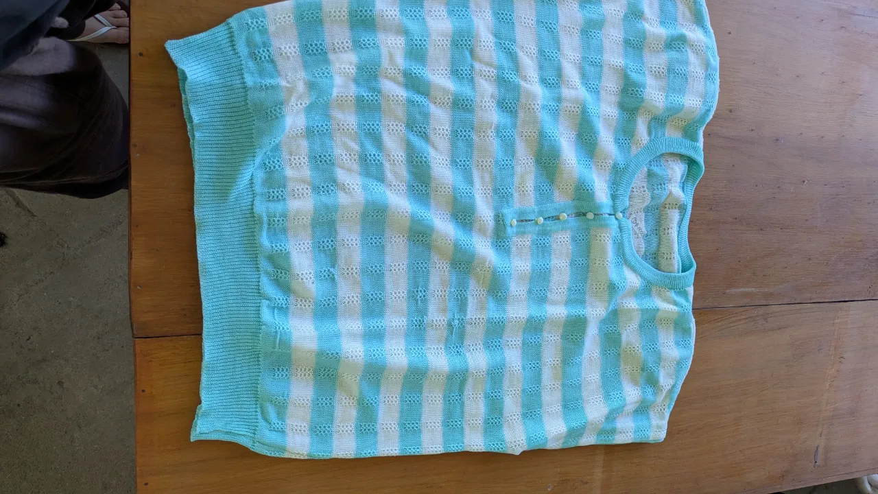 Remera de tejido a cuadros en tonos celeste y blanco, con botones en el cuello y hombreras. Ideal para un look casual y fresco.