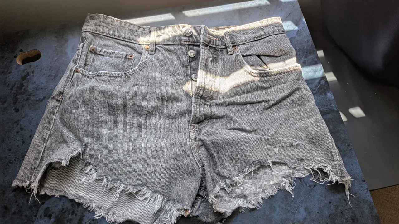 Short de jean ZARA gris con detalles rotos y desflecado. Tiro medio, con botones y bolsillos.