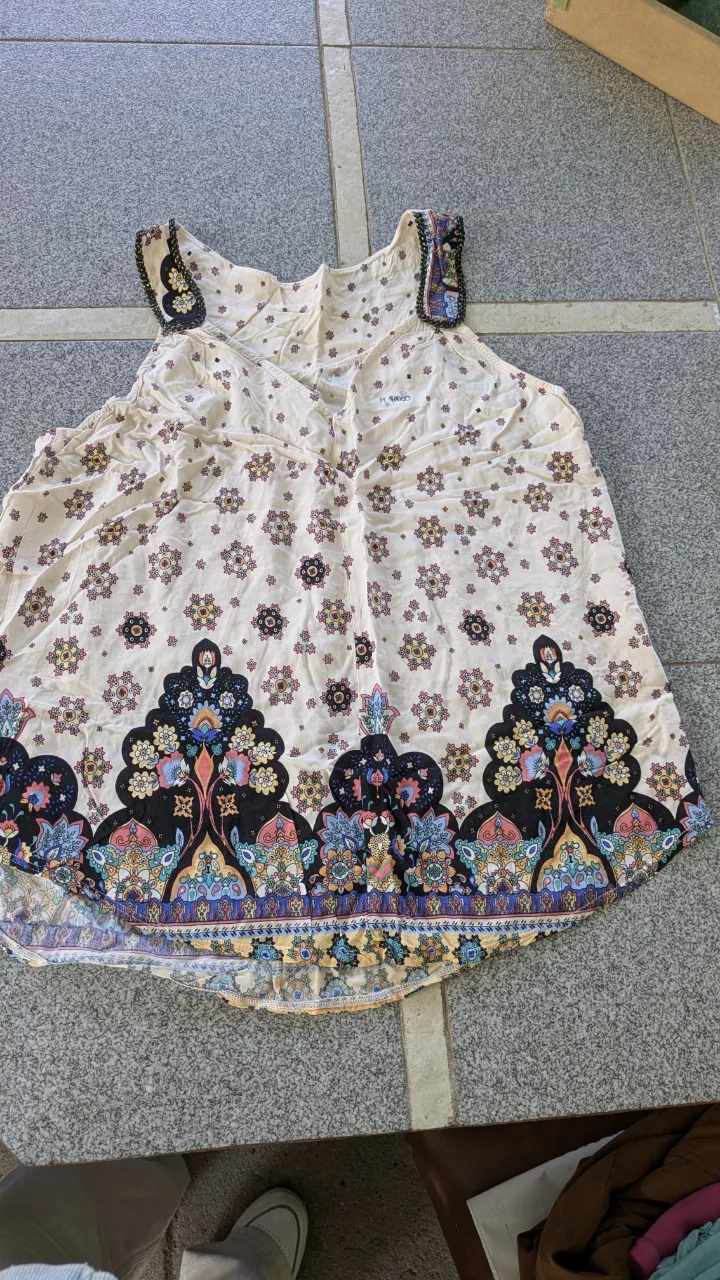 Remera sin mangas, escote en V, con estampa floral y geométrica en la parte inferior. Los breteles tienen un detalle de borde negro con hilo dorado.