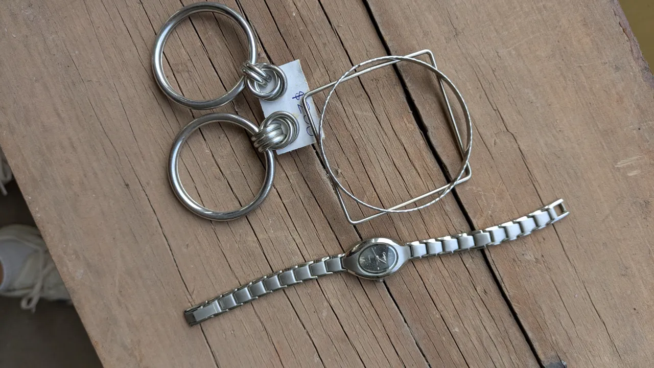 Set de accesorios de metal plateado: dos aros grandes con eslabones, un brazalete con diseño cuadrado y un reloj con malla metálica sin pila.