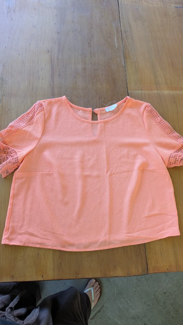 Blusa color coral con mangas cortas de encaje y detalles calados en la espalda. Ideal para un look casual y fresco.