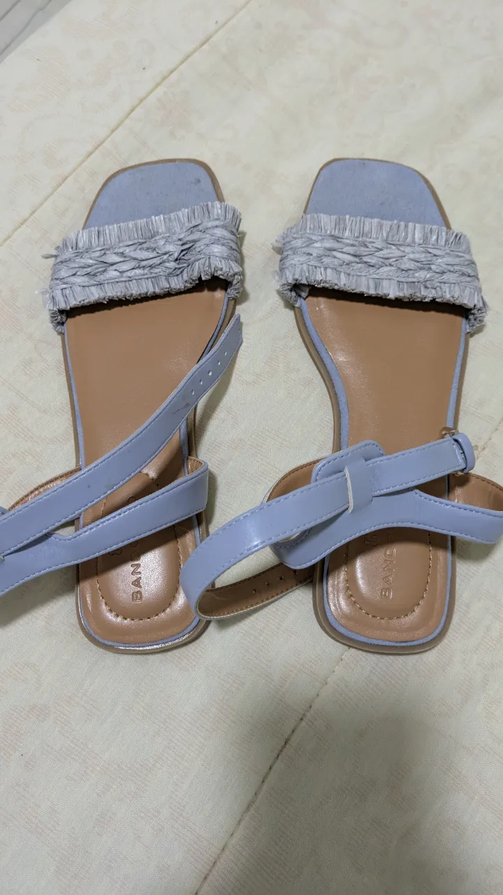 Sandalias planas celestes con detalle de flecos en la capellada. Tiras finas y hebilla para ajustar en el tobillo. Suela marrón claro. Marca Bandolino.