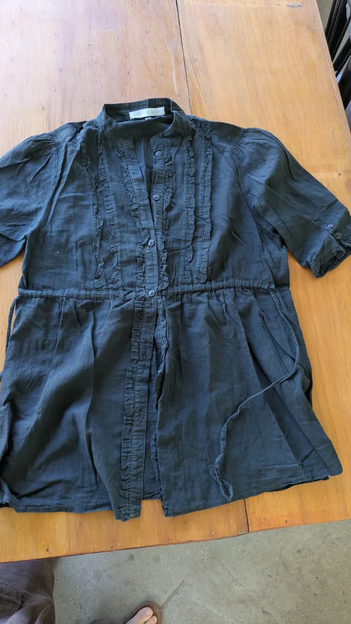 Camisa negra de lino con detalles de volados y cordón para ajustar en la cintura. Ideal para un look casual y chic.