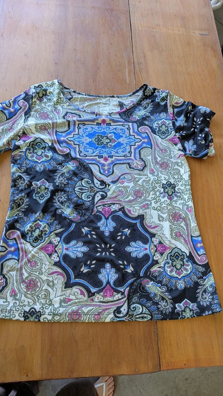 Remera estampada con un diseño paisley y floral en tonos azules, rosas, negros y blancos. Posee mangas cortas y cuello redondo. Ideal para un look casual y vibrante.