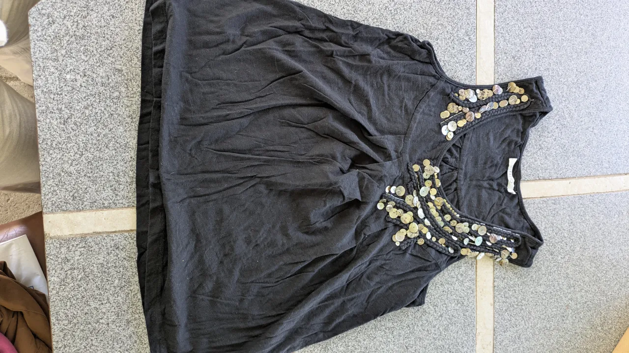 Musculosa negra con detalles de apliques circulares y trenzados en el escote. Los apliques son de material nacarado y metalizado, con un diseño que evoca botones.