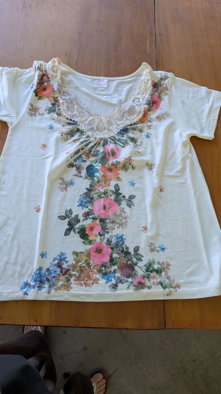 Remera blanca con estampa floral vibrante y detalles de encaje en el cuello. Ideal para un look fresco y femenino.