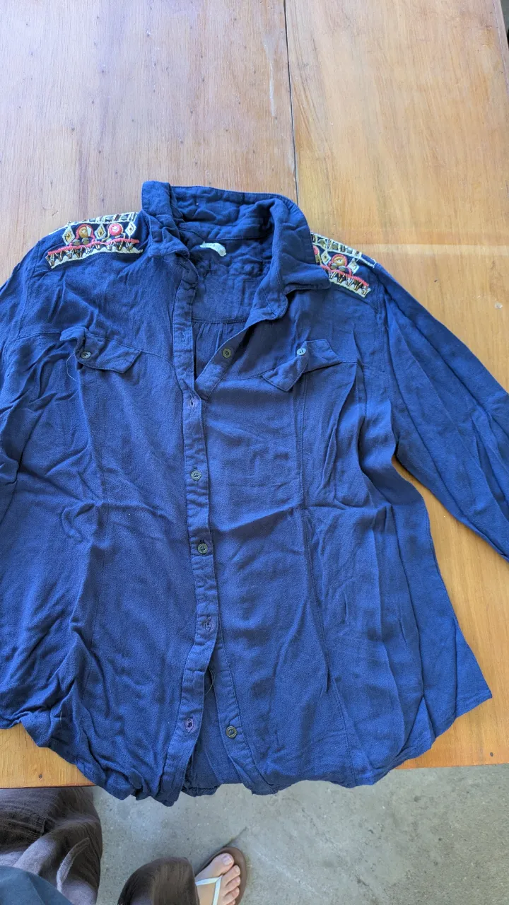 Camisa de jean azul con bordados coloridos en los hombros y la espalda. Posee botones al frente y bolsillos en el pecho. Ideal para un look casual y canchero.