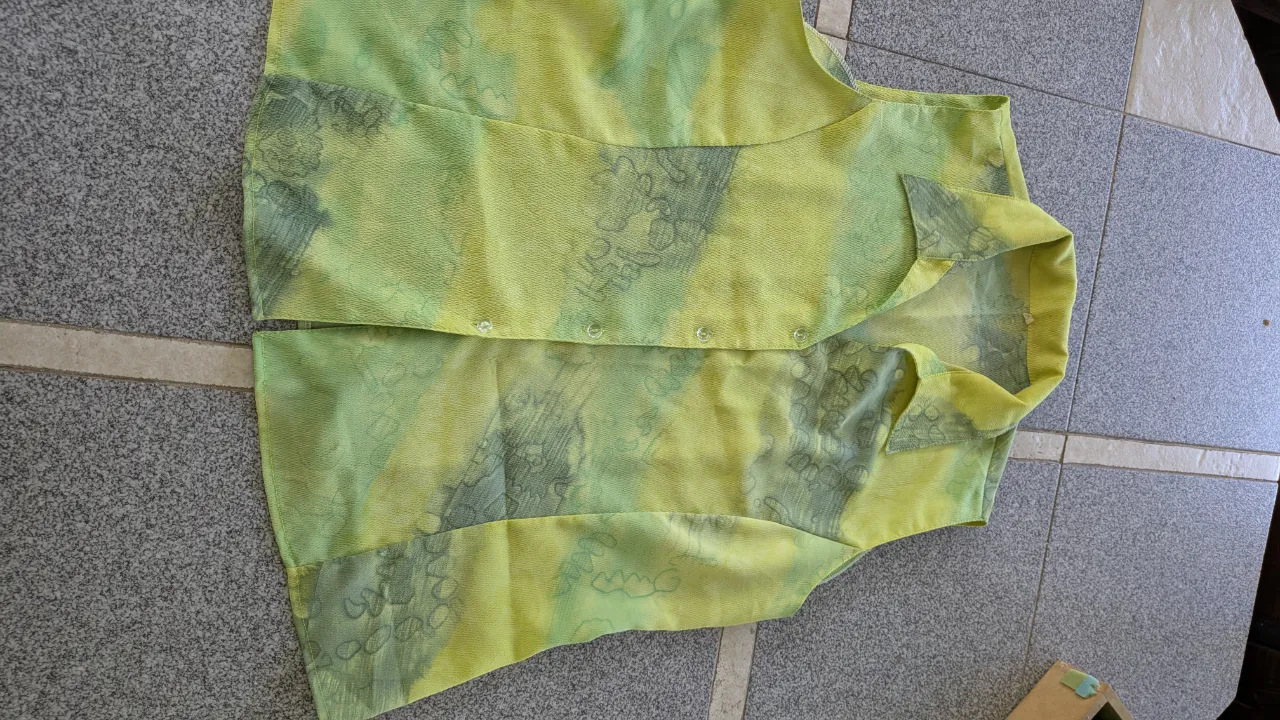 Remera/ camisa musculosa de seda estampada con motivos abstractos en tonos verdes y grises. Posee cuello camisero y botones al frente.