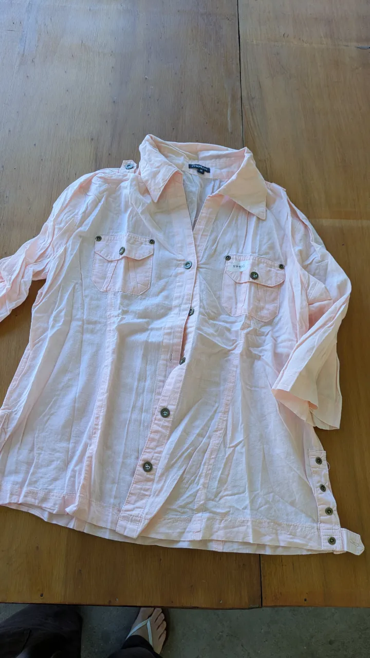 Camisa rosa pastel de manga larga con botones al frente y dos bolsillos en el pecho. Detalle de botones en los puños y en los laterales inferiores. Perfecta para un look casual y fresco.