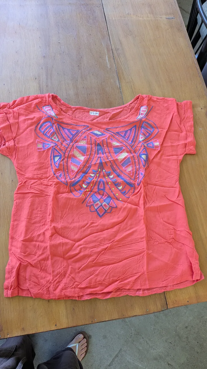 Remera coral con estampa geométrica bordada en el frente. Diseño vibrante y original, ideal para darle un toque canchero a tu look.