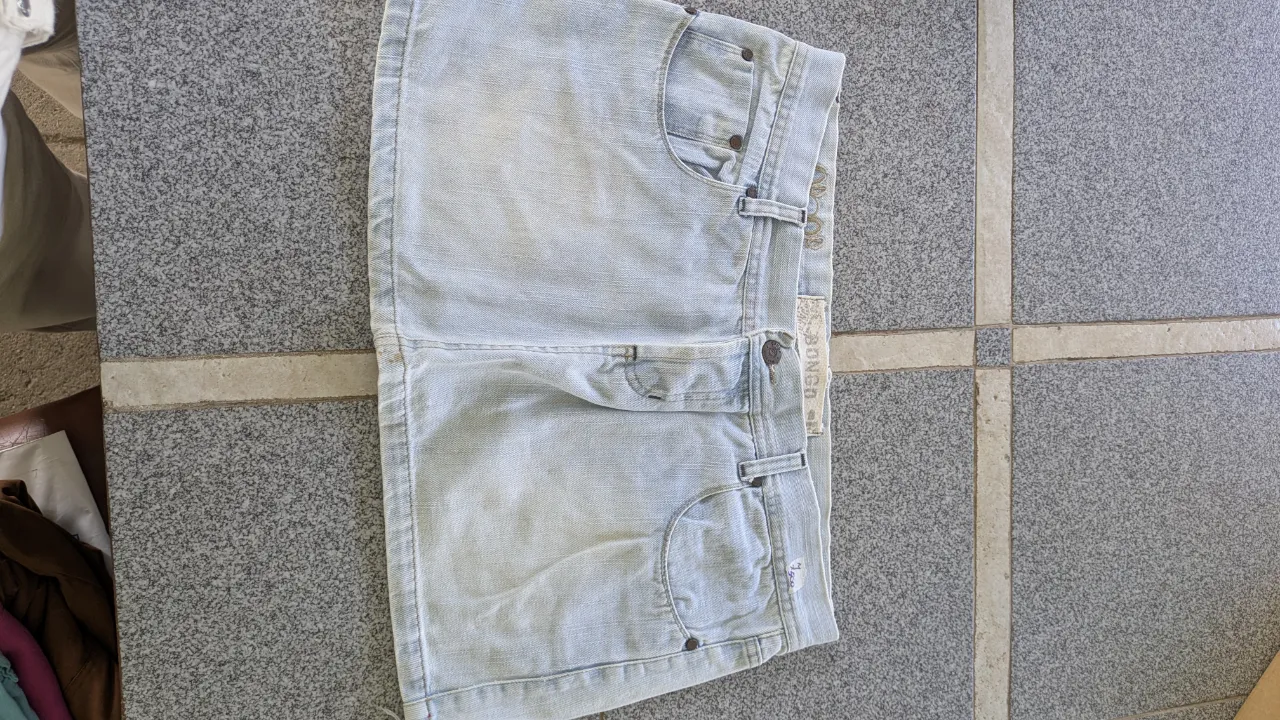 Pollera de jean tiro alto, color celeste. Tiene bolsillos delanteros y traseros. Presenta costuras rojas y detalles bordados en uno de los bolsillos.