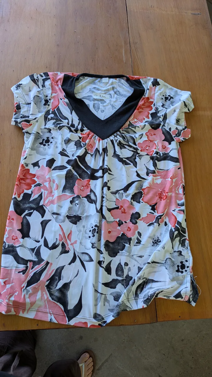 Remera estampada con flores en tonos rosas, blancos y negros. Posee un escote en V con un detalle de tela negra.